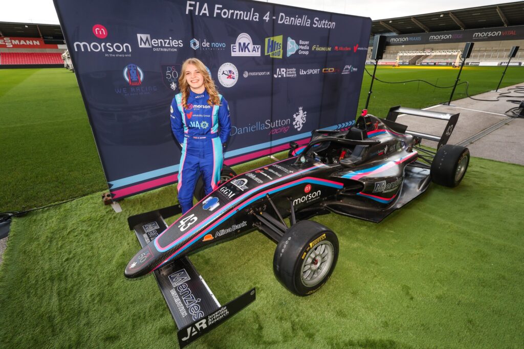 Daniella now, standing next to a Formula 4 race car