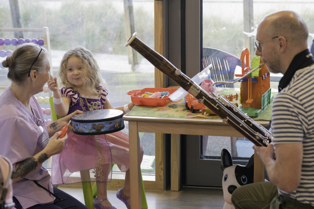 Alder Hey Play Specialised and Arts for Health representative with a young girl playing musical instruments