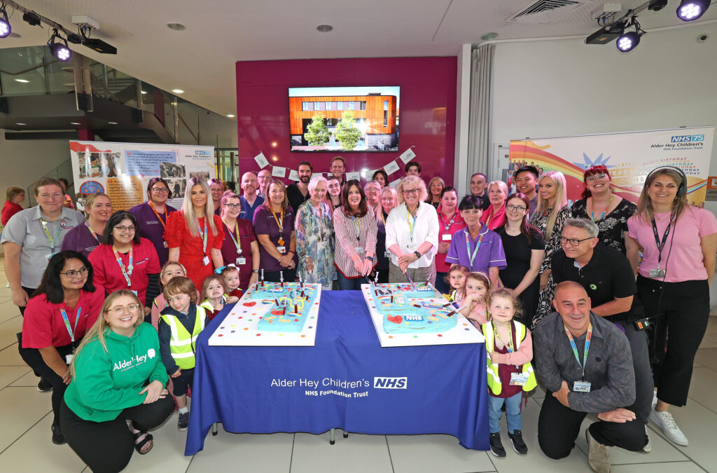 Group photo of people celebrating 75 years of the NHS with a cake