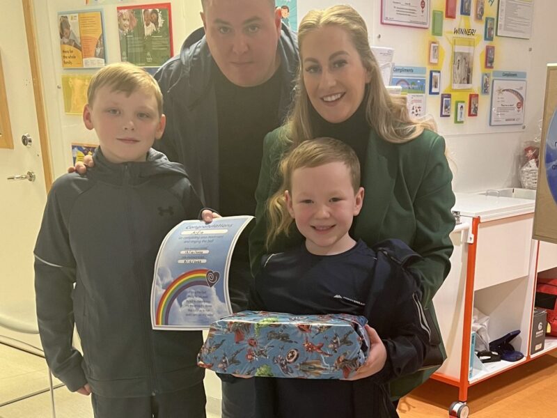 Two parents and children smile with a certificate and a gift