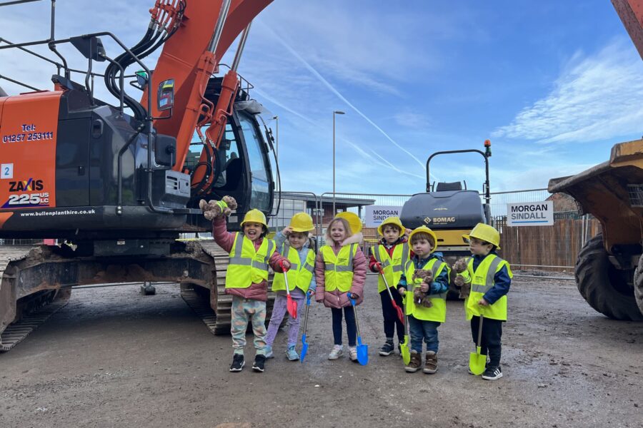 Members of the Alder Hey Nursery post next to a digger holding toy spades and wearing PPE.