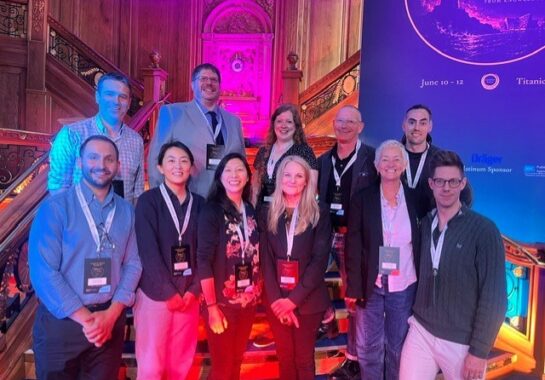 A group of colleagues posing together on a staircase under colourful event lighting.