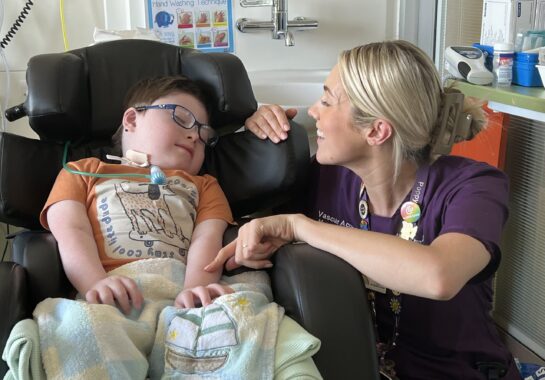 Child in chair with smiling nurse next to them