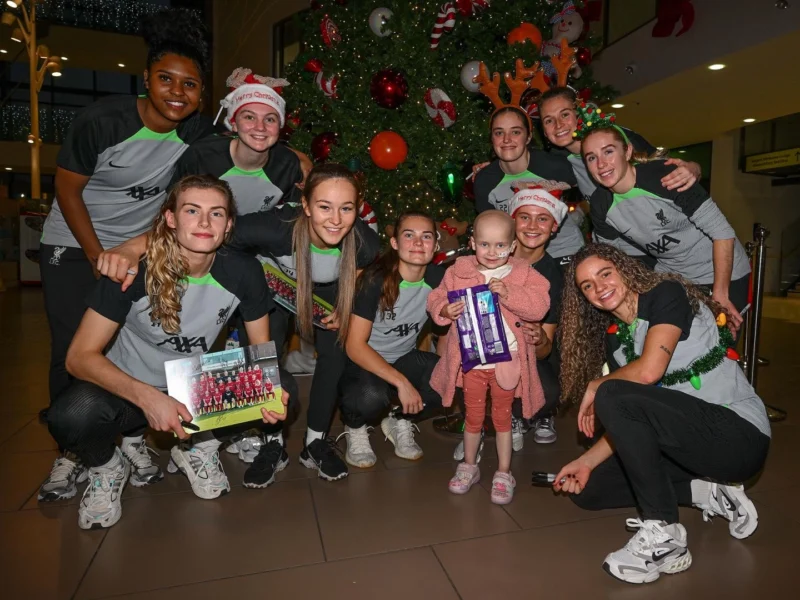 Picture of a little girl holding Christmas selection boxes with players from LFC Women's first team.