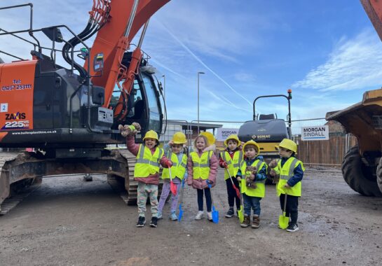 Members of the Alder Hey Nursery post next to a digger holding toy spades and wearing PPE.